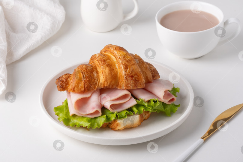 Скачать Круассан с ветчиной и листьями салата подается с чашкой какао на белом столе фотосток Ozero