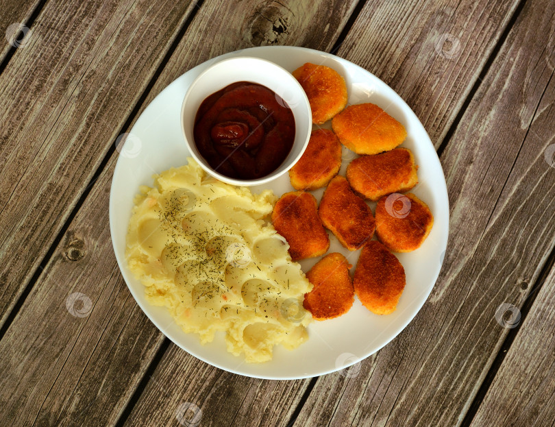 Скачать Картофельное пюре, жареные куриные наггетсы и чашка томатного соуса в круглой тарелке на деревянном столе. фотосток Ozero