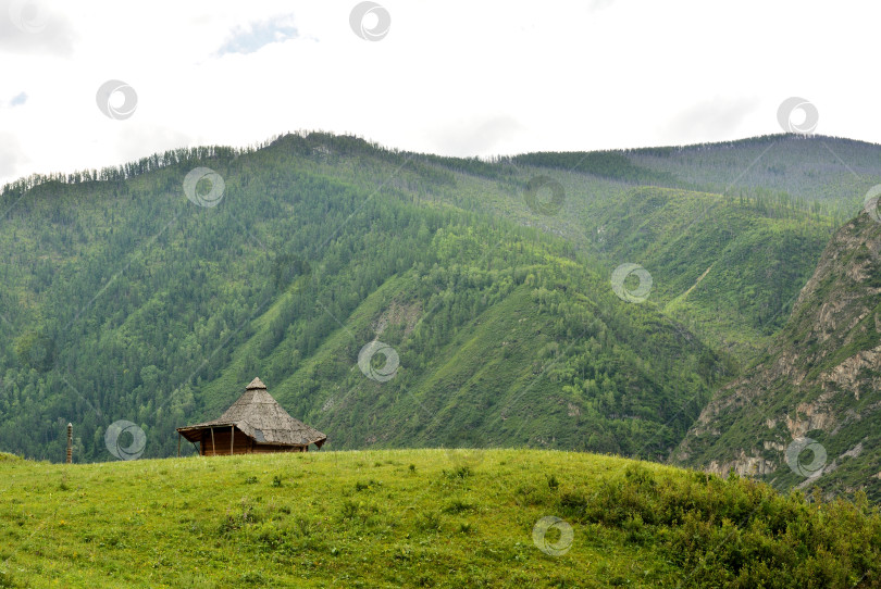 Скачать Традиционный алтайский национальный жилой дом расположен на вершине холма, откуда солнечным летним днем открывается вид на горные вершины. фотосток Ozero