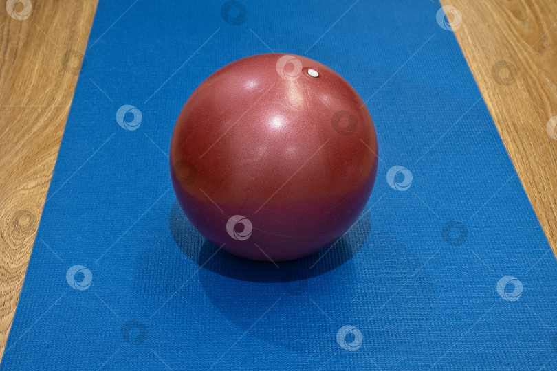 Скачать Красный мяч для упражнений, положенный на синий коврик для йоги в тренажерном зале во время утренней тренировки для любителей фитнеса фотосток Ozero