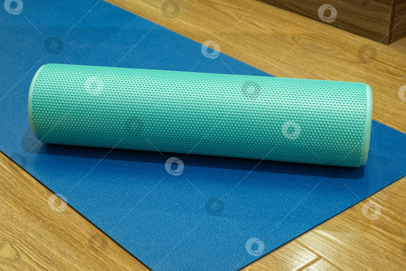 Скачать Поролоновый валик, положенный на синий коврик для йоги в фитнес-центре, для растяжки и восстановления после тренировки фотосток Ozero