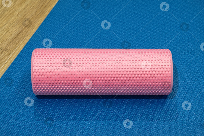 Скачать Поролоновый валик, положенный на синий коврик для йоги в фитнес-центре, для растяжки и восстановления после тренировки фотосток Ozero