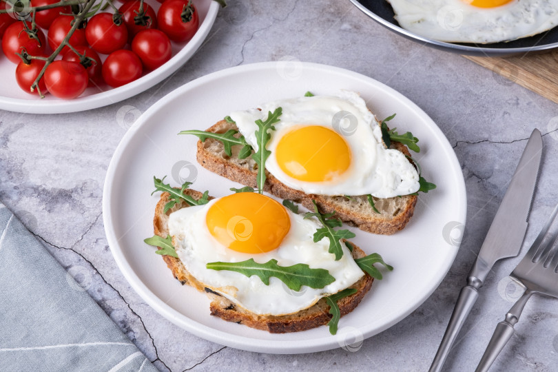Скачать Завтрак с яйцами на тостах и свежей рукколой подается на белой тарелке на кухне фотосток Ozero