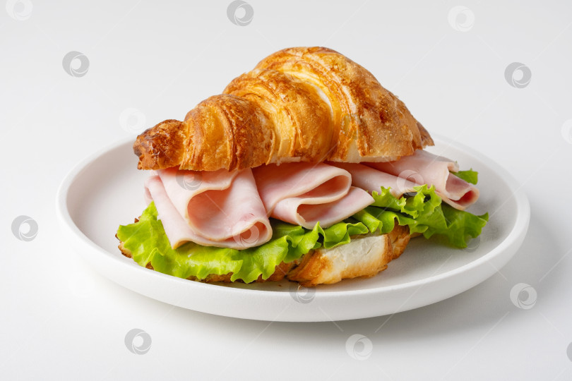 Скачать Круассан с ветчиной и листьями салата подается на белой тарелке фотосток Ozero