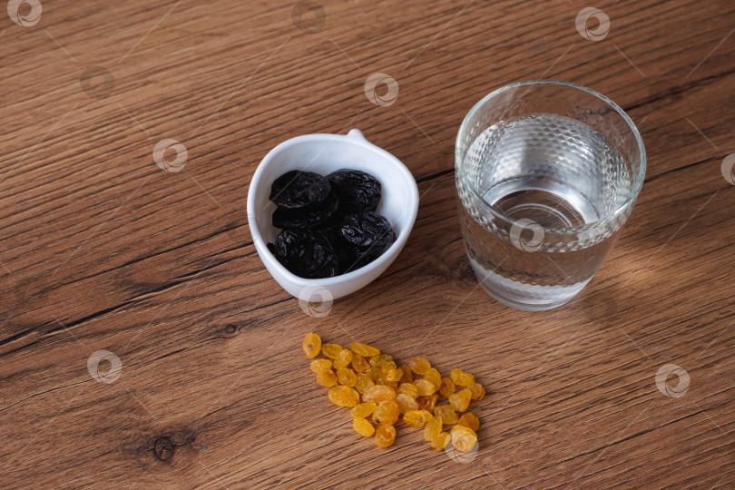 Скачать простой натюрморт со стаканом воды, изюмом и черносливом, стоящим на деревянном столе перед ифтаром в Рамадан фотосток Ozero