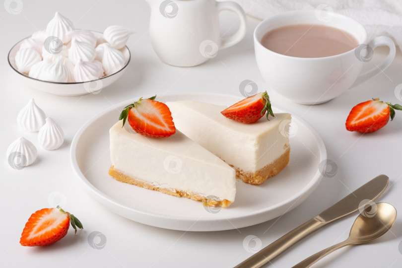 Скачать Вкусный чизкейк подается с клубникой и чашечкой горячего напитка на простом белом столе фотосток Ozero