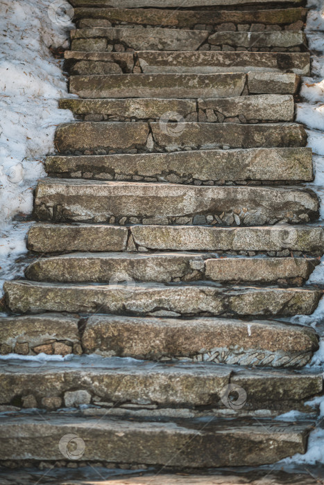 Скачать Каменные ступени, спускающиеся наружу, частично покрыты белым снегом и скользким льдом, образуя сложную дорожку в холодное зимнее время года, иллюстрирующую темы природы и архитектуры. фотосток Ozero