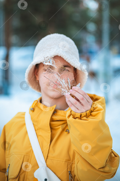 Скачать Человек в желтой куртке и кремовой шляпе, держащий голыми руками сверкающий кусочек кристаллического льда на размытом естественном фоне улицы, отражающий солнечный свет и ощущающий холод фотосток Ozero