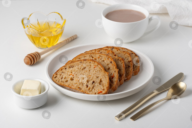Скачать Свеженарезанный хлеб подается с маслом, медом и теплым напитком в простой обстановке в утренние часы. фотосток Ozero
