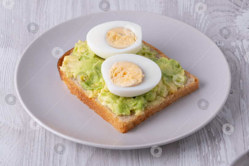 Скачать Вкусные тосты с пюре из авокадо и нарезанными ломтиками вареными яйцами подаются на тарелке фотосток Ozero