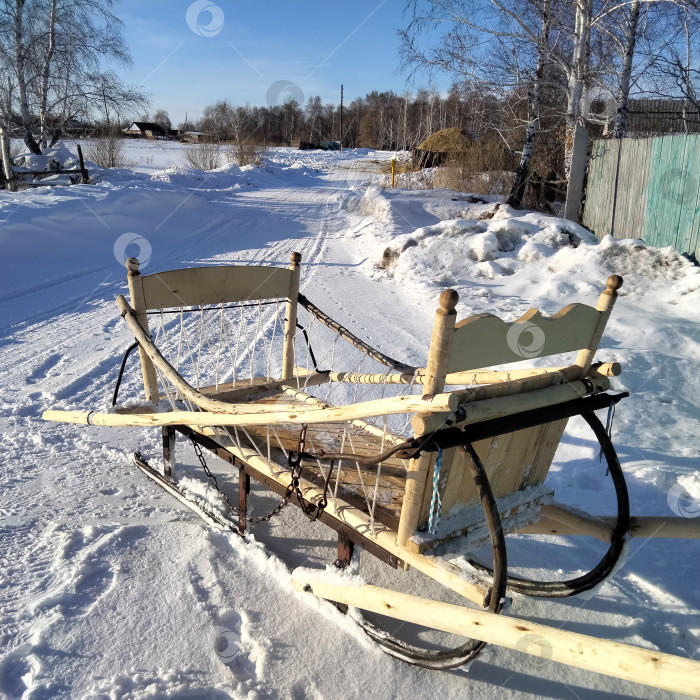 Скачать Сани деревянные новые дровни на металлических полозьях ручной работы, крупный план на заснеженной дороге. фотосток Ozero