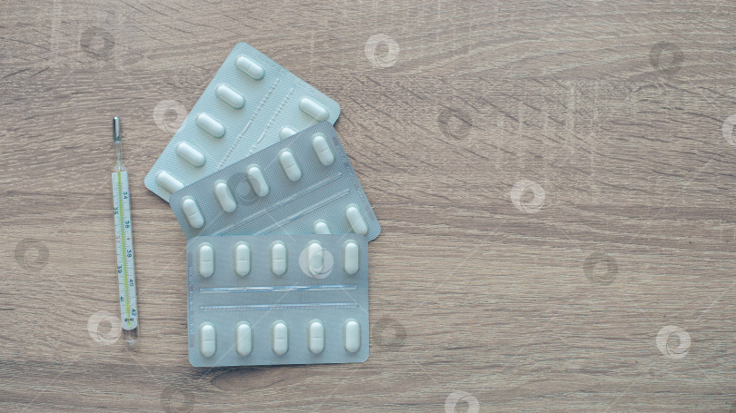 Скачать Таблетки, градусник, обезболивающие на деревянном столе фотосток Ozero