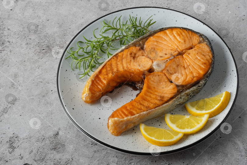 Скачать Обжаренный стейк из лосося с розмарином и кусочками лимона на сером столе фотосток Ozero