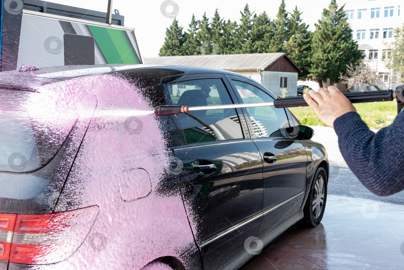 Скачать Водитель-Мужчина Наносит Розовую Пену На Черную автомойку На Автомойке Для Ухода За Автомобилем фотосток Ozero