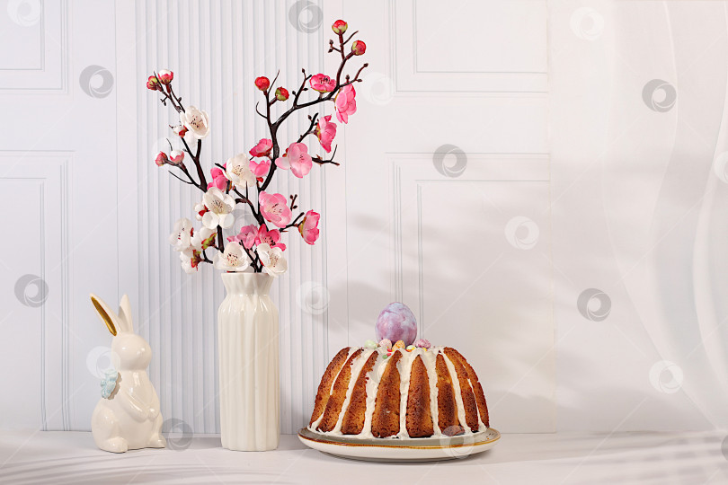 Скачать Традиционный пасхальный кулич, фигурки пасхальных кроликов и ветки сакуры в вазе на фоне элегантной кухни, концепция празднования Пасхи, идеи пасхальных блюд для домашней кухни, шаблон дизайна фотосток Ozero