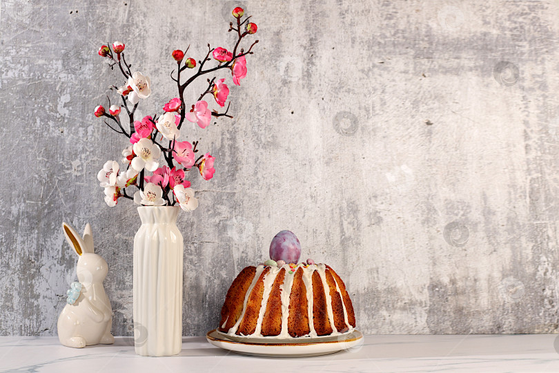 Скачать Традиционный пасхальный кулич, фигурки пасхальных кроликов и ветки сакуры в вазе на фоне элегантной кухни, концепция празднования Пасхи, идеи пасхальных блюд для домашней кухни, шаблон дизайна фотосток Ozero