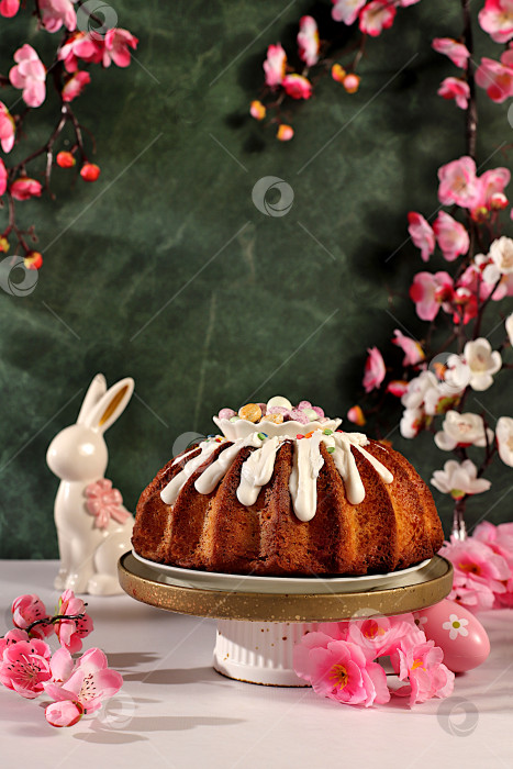 Скачать Традиционный пасхальный кулич, фигурки пасхальных кроликов и ветки сакуры в вазе на фоне элегантной кухни, концепция празднования Пасхи, идеи пасхальных блюд для домашней кухни, шаблон дизайна фотосток Ozero