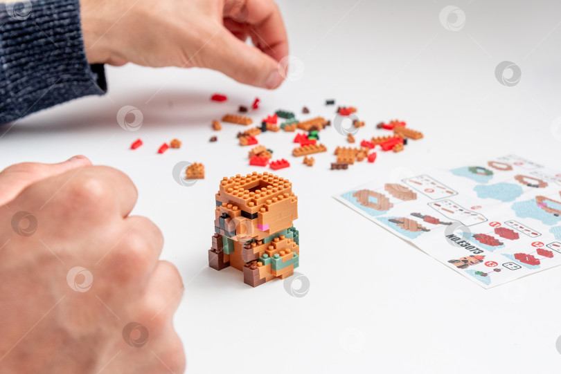 Скачать Бар, Черногория, 20 марта 2026 года, Мужчина играет в конструктор Lego с фигуркой животного капибары фотосток Ozero