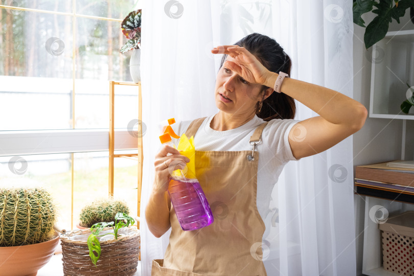 Скачать Домохозяйка в фартуке испытывает эмоциональное выгорание, хлопочет у окна, испытывает стресс, оранжевые перчатки, прикладывает руку ко лбу, нуждается в профессиональной помощи, рекламный ролик сервисного бизнеса фотосток Ozero
