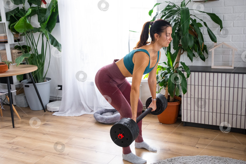 Скачать Женщина приседает с гантелями, фитнес дома, спортивная одежда, тренировочный коврик, минималистичная комната с растениями, здоровые привычки, силовые тренировки, спорт в помещении фотосток Ozero