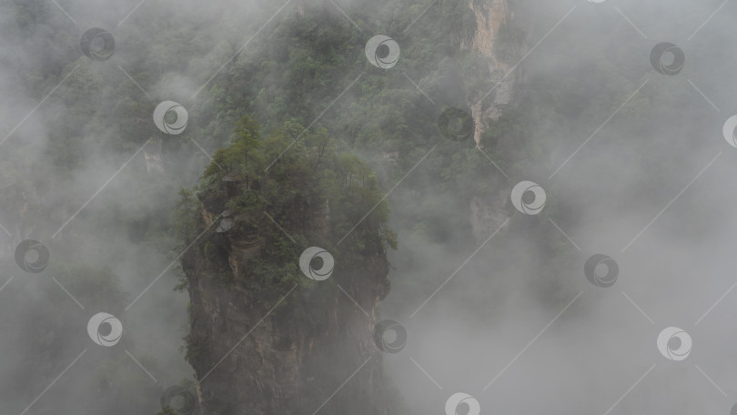 Скачать Туманный горный пейзаж. Высокий каменный столб окутан туманом и облаками. фотосток Ozero