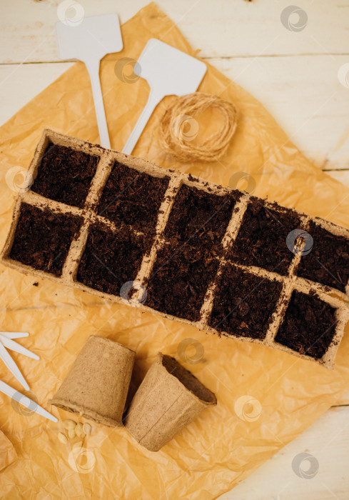 Скачать Вид сверху на семена и ячейки с почвой на деревянном фоне. Выращивание рассады в торфяных стаканчиках. Концепция весеннего озеленения дома. фотосток Ozero