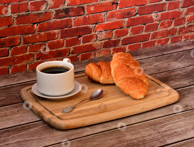 Скачать Деревянный поднос с двумя свежими круассанами и чашкой горячего черного кофе на деревянном столе. фотосток Ozero