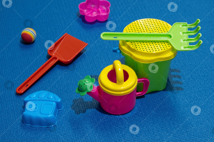 Скачать В солнечный день дети играют с разноцветными пластиковыми игрушками на синем коврике фотосток Ozero