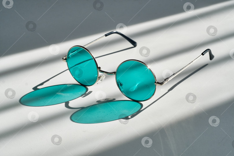 Скачать Стильные круглые солнцезащитные очки с бирюзовыми линзами в ярком солнечном свете с графичными тенями фотосток Ozero