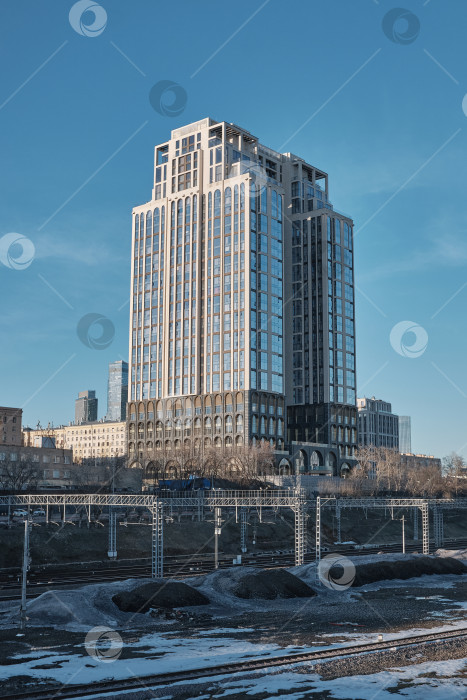 Скачать Москва, Россия, 22.03.2026. Современный элитный жилой комплекс с панорамным остеклением и арочными фасадами на фоне синего неба. фотосток Ozero