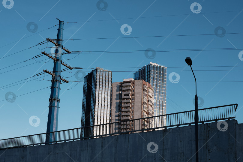 Скачать Москва, Россия, 22.03.2026. Городской пейзаж с современными небоскребами, опорой ЛЭП и бетонным мостом на фоне синего неба фотосток Ozero