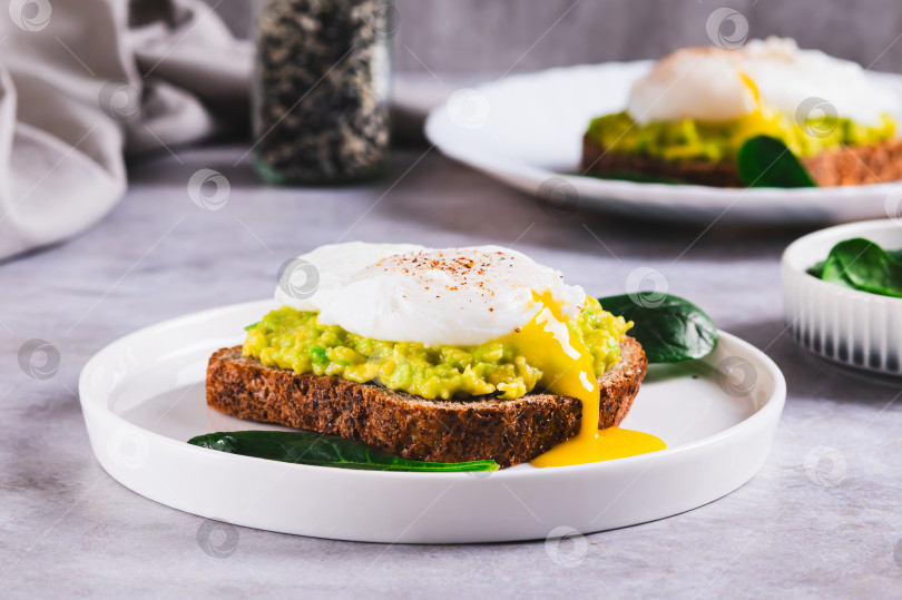 Скачать Ржаной хлеб с гуакамоле и яйцом-пашот на тарелке на столе фотосток Ozero