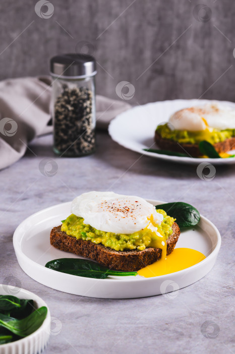 Скачать Ржаной хлеб с гуакамоле и яйцом-пашот на тарелке на столе, вид сверху фотосток Ozero