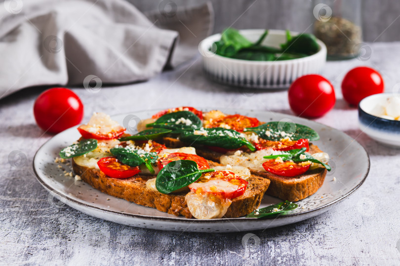 Скачать Запеченные бутерброды с моцареллой, помидорами и шпинатом на тарелке на столе фотосток Ozero