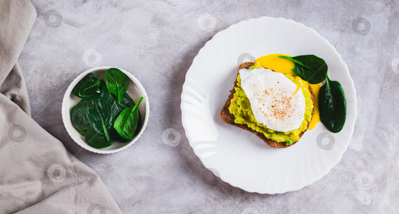 Скачать Сэндвич с авокадо, яйцом-пашот и шпинатом на тарелке вид сверху веб-баннер фотосток Ozero