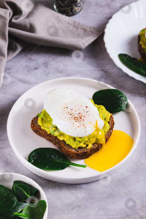 Скачать Сэндвич с авокадо, яйцом-пашот и шпинатом на тарелке на столе, вид сверху фотосток Ozero