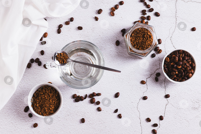 Скачать Чашка с водой, гранулы растворимого кофе и кофейные зерна на столе вид сверху фотосток Ozero