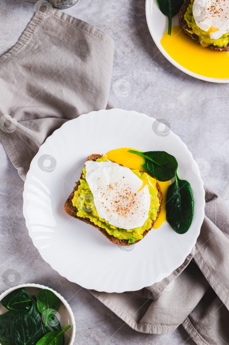 Скачать Сэндвич с авокадо, яйцом-пашот и шпинатом на тарелке в вертикальном положении фотосток Ozero