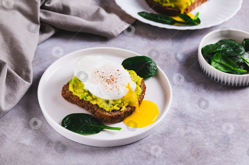 Скачать Бутерброд с авокадо, яйцом-пашот и шпинатом на тарелке на столе фотосток Ozero