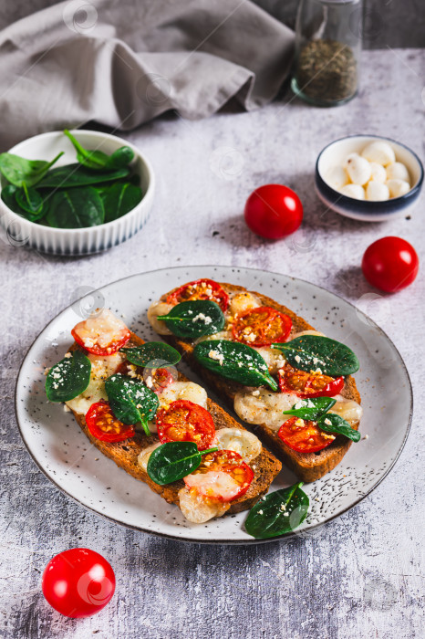 Скачать Запеченная брускетта с салатом капрезе и шпинатом на тарелке на столе, вид сверху фотосток Ozero