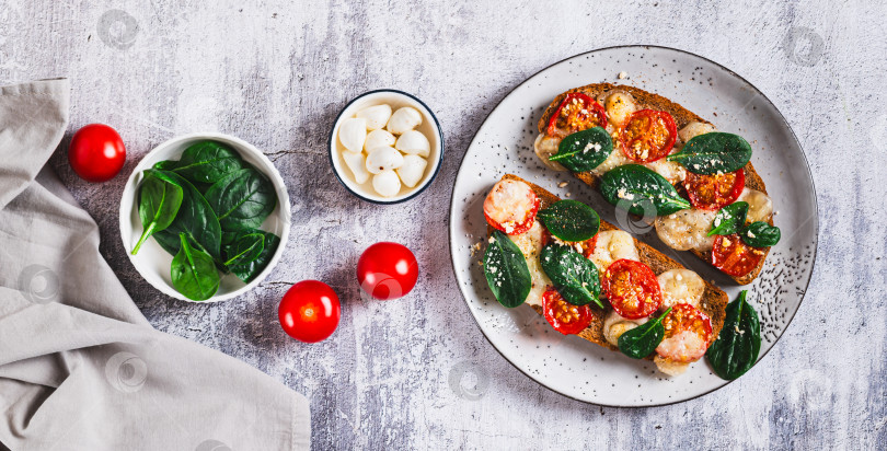 Скачать Запеченная брускетта с салатом капрезе и шпинатом на тарелке на столешнице посмотреть веб-баннер фотосток Ozero