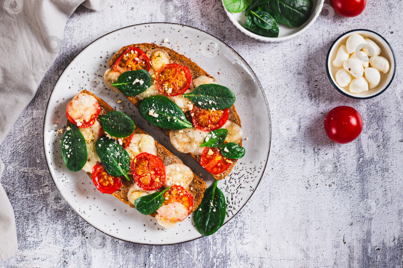 Скачать Запеченные бутерброды с моцареллой, помидорами и шпинатом на тарелке, вид сверху фотосток Ozero