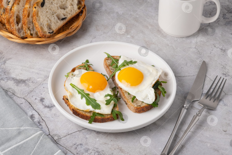 Скачать Завтрак с яйцами на тостах и свежей рукколой подается на белой тарелке на кухне. фотосток Ozero