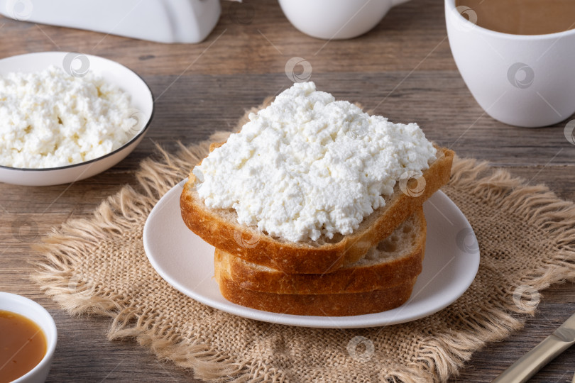 Скачать Сервировка завтрака с хлебом, творогом, кофе и джемом на деревянном столе в уютной кухонной обстановке фотосток Ozero