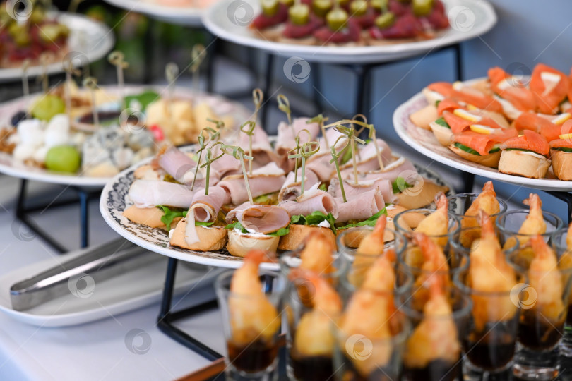 Скачать Ассорти из закусок для кейтеринга с креветками, темпурой и мясной брускеттой на фуршетном столе для украшения мероприятия в отсутствие людей и свободного пространства для копирования фотосток Ozero