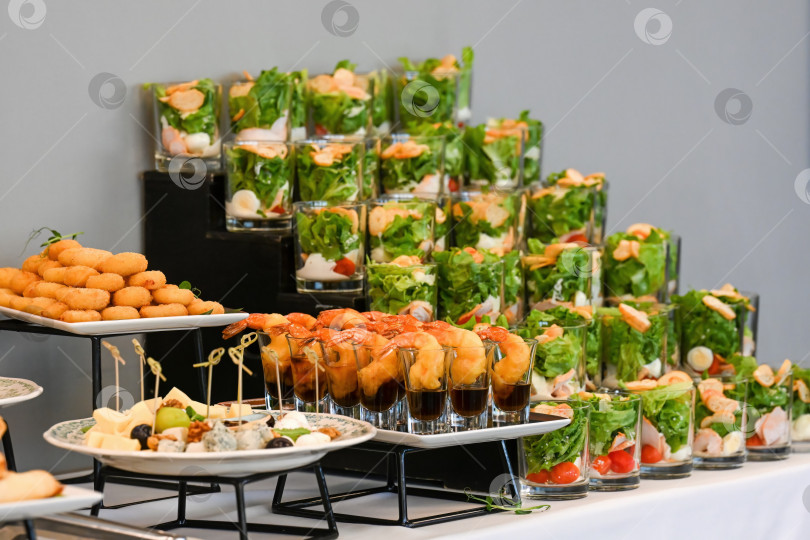Скачать Ассорти закусок для кейтеринга с салатом из креветок в бокале и сырным ассорти на фуршетном столе для украшения мероприятия или вечеринки без людей и свободного пространства для копирования фотосток Ozero