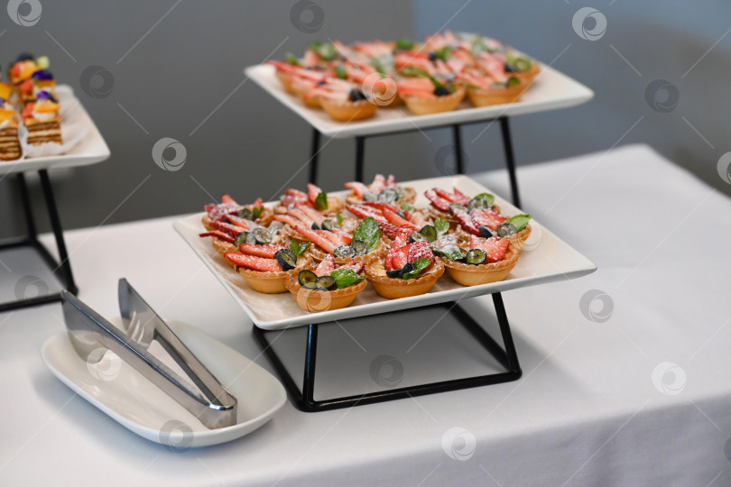 Скачать Ассорти из десертов для кейтеринга с клубничным и чернично-фруктовым пирогом на фуршетном столе для украшения мероприятия или вечеринки в отсутствие людей и свободного пространства. фотосток Ozero