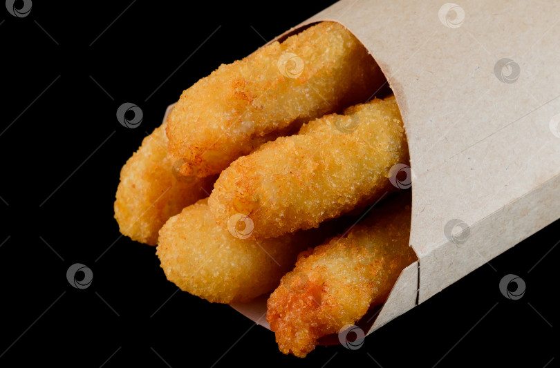 Скачать Хрустящая палочка жареного сыра в кармашке из эко-крафт-бумаги на черном фоне, вид сбоку, крупным планом, вкусная, пикантная нездоровая пища на вынос фотосток Ozero