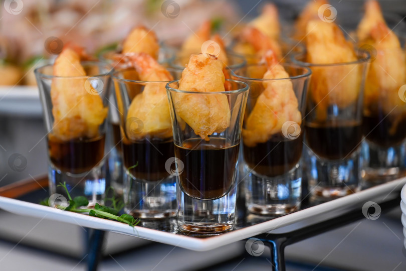 Скачать Кейтеринг-закуска из креветок темпура в стеклянной таре с соевым соусом на фуршетном подносе для украшения мероприятия или вечеринки в отсутствие людей и свободного пространства. фотосток Ozero