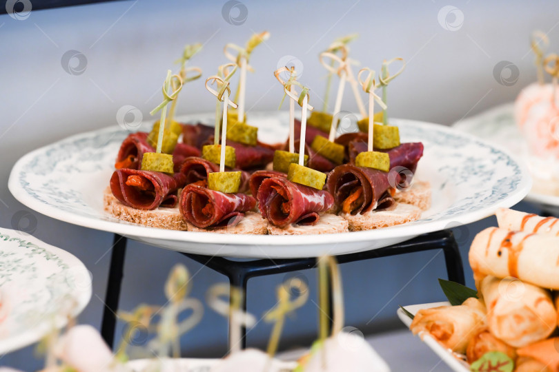 Скачать Закуска для кейтеринга с канапе из говядины брезаола и корнишонами на шпажке для украшения мероприятия с вкусной пикантной мясной закуской на фуршетном столе вид сбоку фотосток Ozero